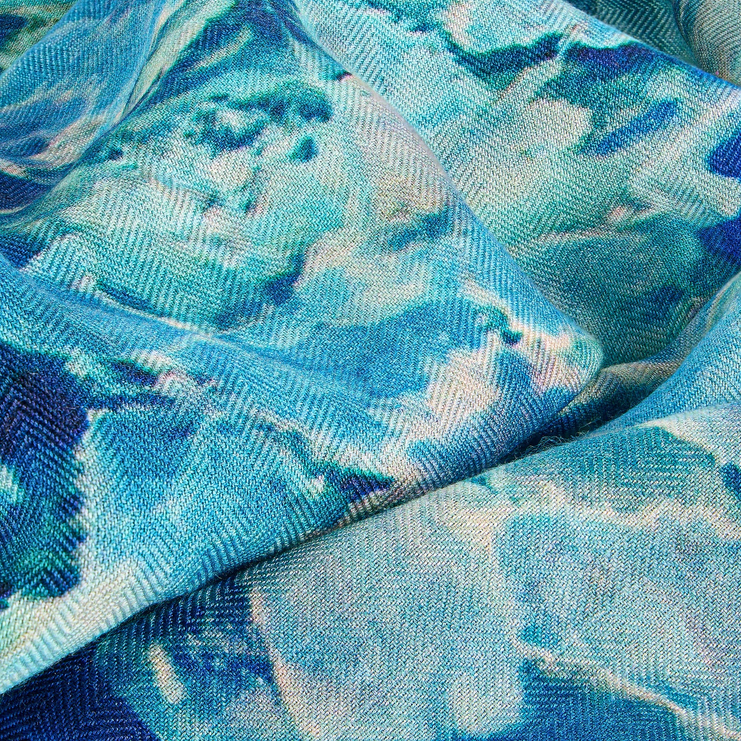 A close-up of an oversized scarf in a soft blend of silk and wool, featuring a dreamy blue color palette with subtle gradient tones. The fabric drapes elegantly, showcasing a luxurious texture that combines warmth and style. Perfect for elevating any outfit while providing comfort and sophistication.