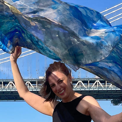 Woman holding the Blue Dream oversized silk chiffon art scarf open in the wind beneath the Manhattan Bridge, 52x52" wearable art by Teascarf Brooklyn