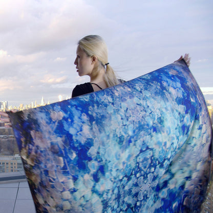 An oversized scarf in a soft blend of silk and wool, featuring a dreamy blue color palette with subtle gradient tones. The fabric drapes elegantly, showcasing a luxurious texture that combines warmth and style. Perfect for elevating any outfit while providing comfort and sophistication. Back view, hands outstretched.