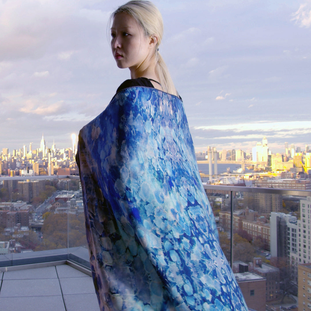 An oversized scarf in a soft blend of silk and wool, featuring a dreamy blue color palette with subtle gradient tones. The fabric drapes elegantly, showcasing a luxurious texture that combines warmth and style. Perfect for elevating any outfit while providing comfort and sophistication. Shoulder view.