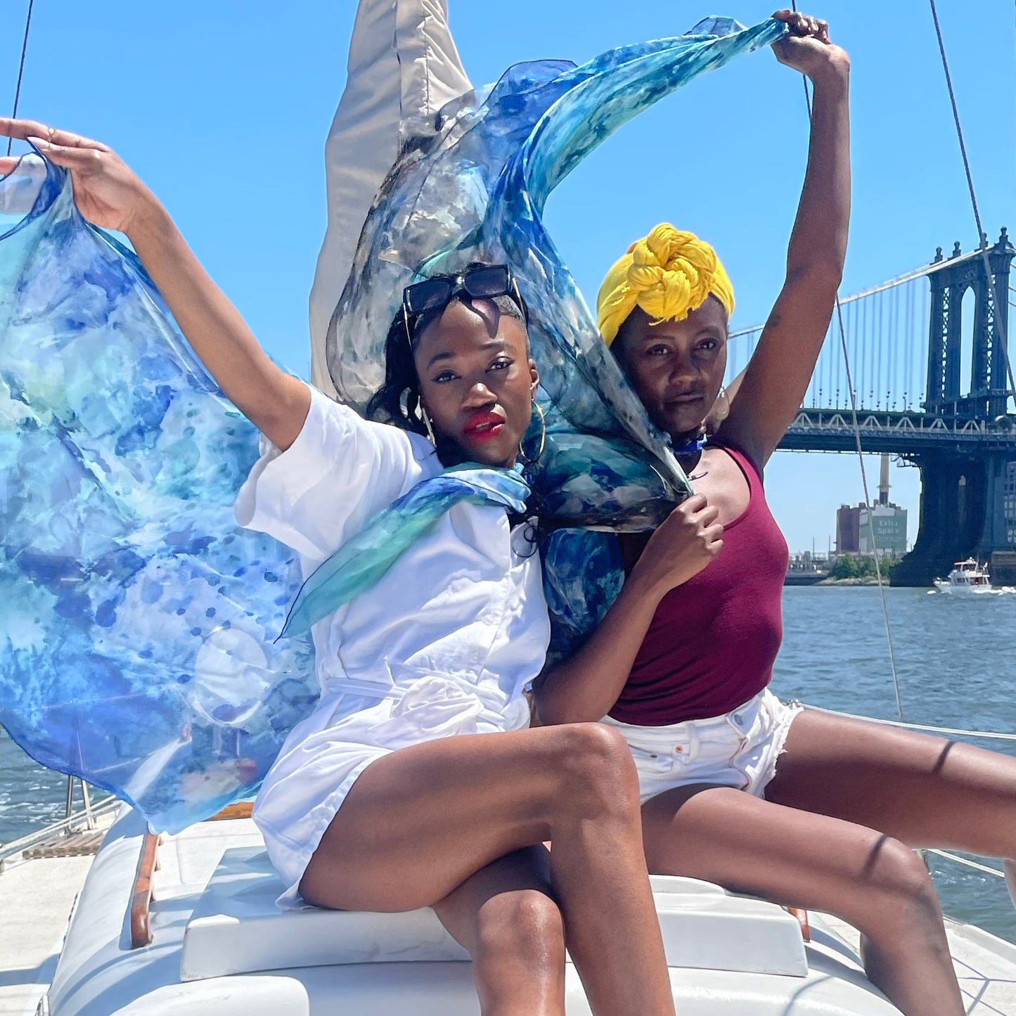 Two models on sailboat holding silk chiffon scarves in the breeze. Manhattan Bridge is visible in background.