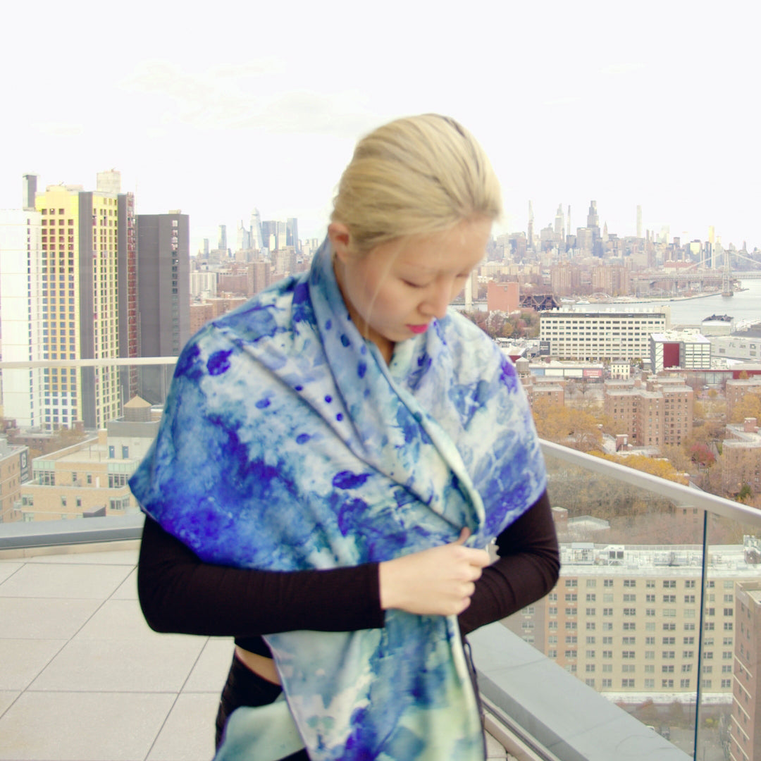 Woman on roof with an oversized silk-wool scarf in a soothing clear blue hue, elegantly draped to showcase its luxurious texture and lightweight design. The scarf features a subtle sheen, enhancing its rich, vibrant color. Perfect for versatile styling, it adds a touch of sophistication to any outfit.