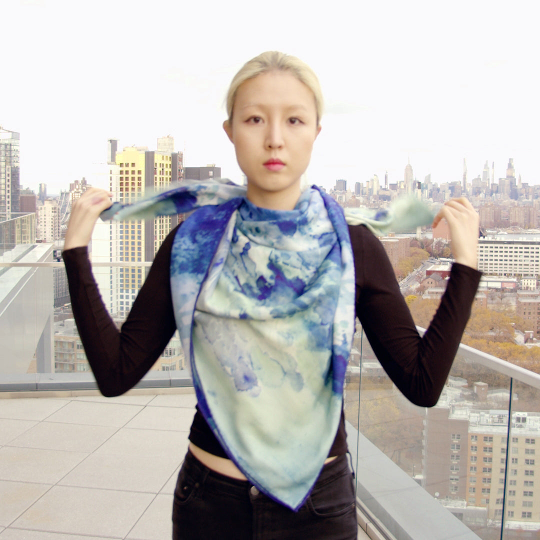 Front view on oversized silk-wool scarf in a soothing clear blue hue, elegantly draped to showcase its luxurious texture and lightweight design. The scarf features a subtle sheen, enhancing its rich, vibrant color. Perfect for versatile styling, it adds a touch of sophistication to any outfit. a model wearing an oversized silk-wool scarf in a soothing clear blue hue, elegantly draped to showcase its luxurious texture and lightweight design. The scarf features a subtle sheen, enhancing its rich, vibrant col