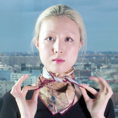 Model stands in front of city view, silk wool scarf is folded diagonally and tied around neck.