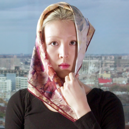 Model stands in front of city view, silk wool scarf is folded diagonally and being draped over head.