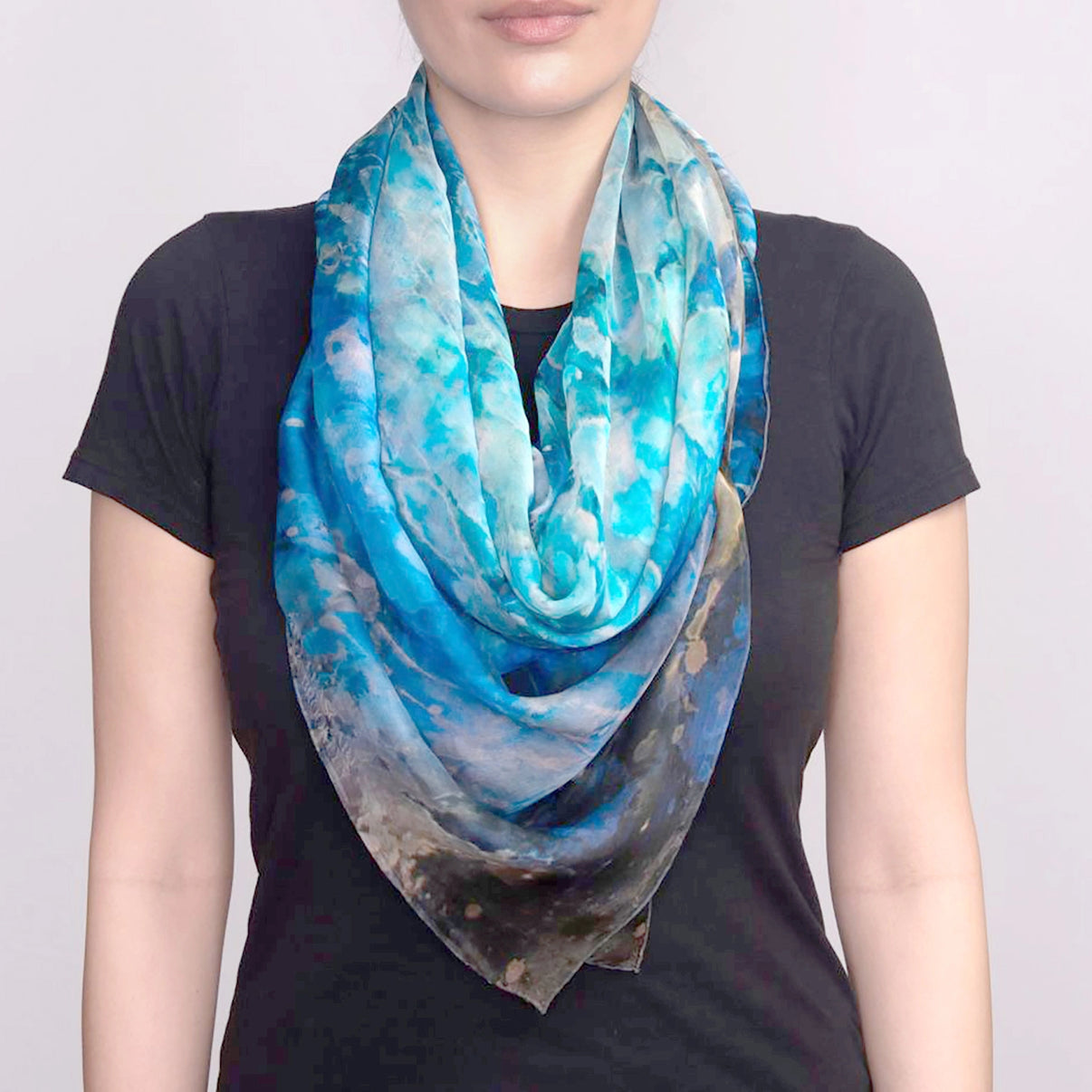 Front view of luxurious, square, silk chiffon, oversized Blue Dream Scarf, folded diagonally, tied loosely around models neck.