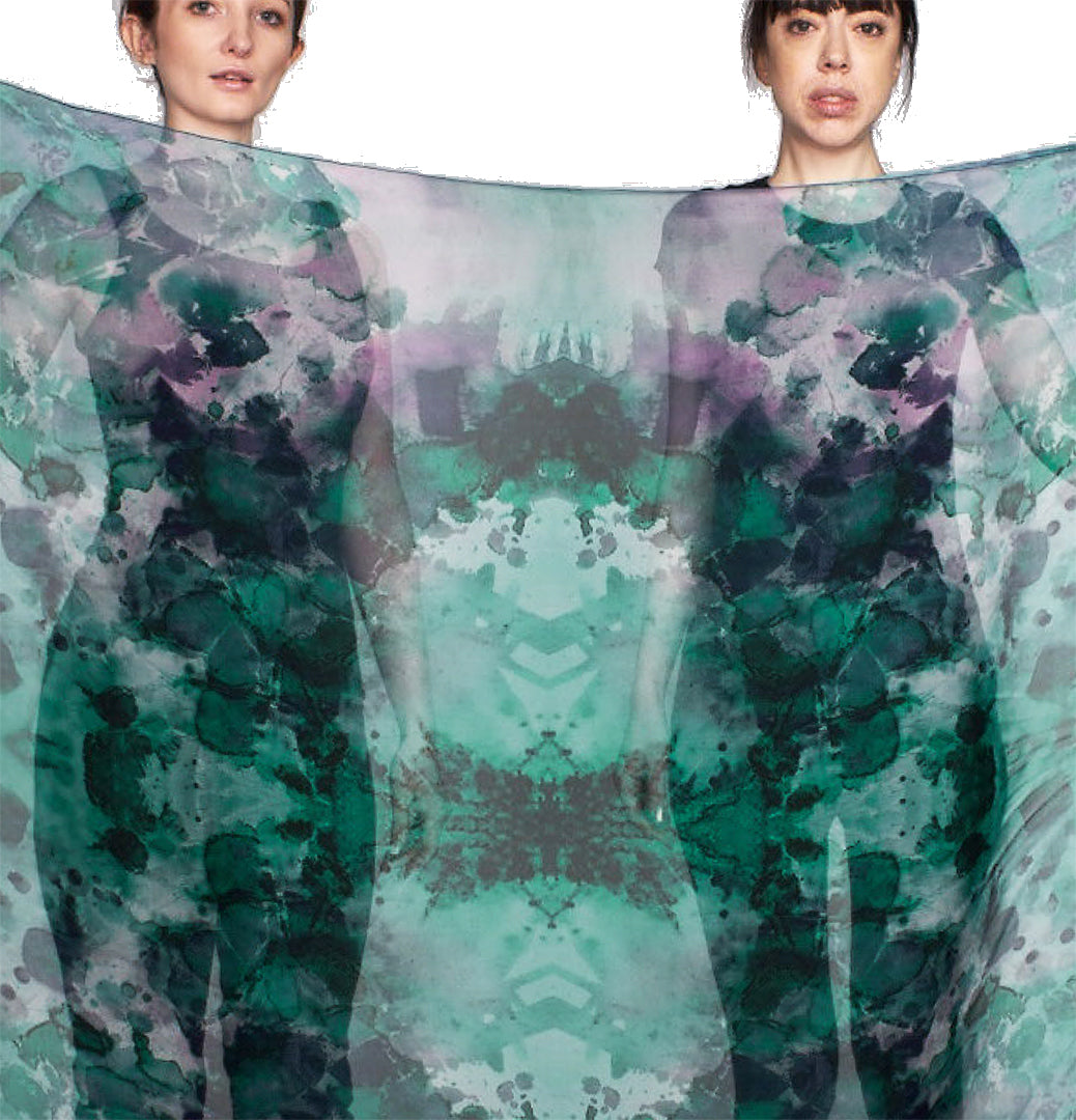 Two models, facing the viewer, holding a sheer scarf in front of them. The vivid color can be seen in their black silhouette..